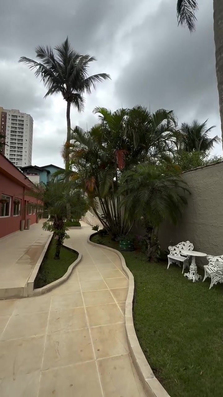 Caminho de pedra da Casa 1 entre o gramado e as palmeiras, com a fachada coral ao fundo.