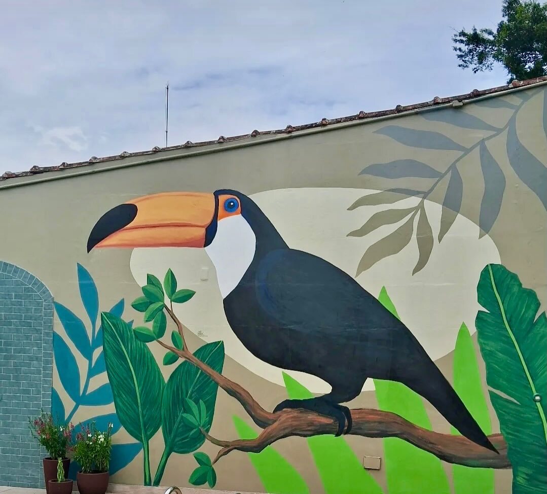 O tucano do mural pintado em tamanho grande sobre um galho, entre folhas de bananeira.